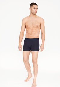 Marineblaue Herren-Boxershorts mit figurbetontem Schnitt, elastischem Bund und glattem Stoff. Modell steht barfuß.