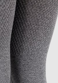 Grijze legging met een gestructureerd patroon, gemaakt van een rekbare stof met een gladde afwerking. Zichtbare naden voegen detail toe.