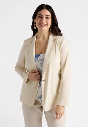 Blazer beige con un singolo bottone, rever a lancia e due tasche, indossato sopra un top a fantasia blu, che trasmette una silhouette leggera e strutturata.