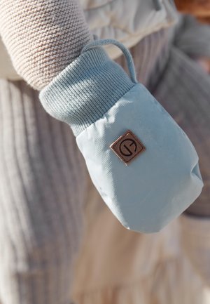 Guanto in tessuto azzurro chiaro con superficie texturizzata e polsino a maglia, con un'etichetta logo marrone. Accompagnato da un maglione in tonalità neutre.