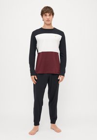 Langarmoberteil in Schwarz, Weiß und Bordeaux mit kleinem Logo auf der Brust, kombiniert mit schwarzen, schmal geschnittenen Hosen. Aus weichem Baumwollstoff.