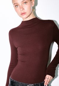 Langsleeve top in donker bordeaux gebreid materiaal met een hoge hals en een aansluitend ontwerp. Heeft een soepele textuur en lange mouwen.