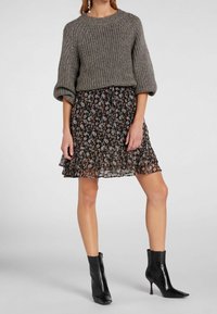Szary dziergany sweter o prążkowanej fakturze, zestawiony z czarną mini spódniczką w kwiatowy wzór. Całość dopełniają czarne botki na obcasie.