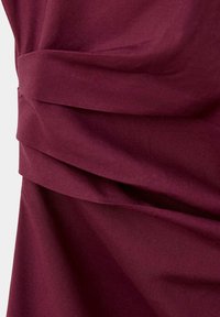 Tissu bordeaux avec des plis doux et un drapé en couches créant des lignes horizontales texturées et superposées.