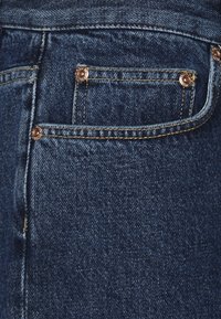 Vaqueros de mezclilla azul oscuro con una textura suave, que cuentan con un bolsillo trasero con herrajes de cobre y detalles de costura dorada.