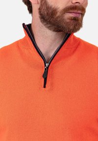 Pull à demi-fermeture éclair orange avec col et poignets côtelés, présentant une fermeture éclair foncée contrastante. Texture douce et coupe ajustée.
