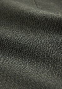 Tessuto strutturato in verde scuro, con un motivo intrecciato e sottili variazioni di colore, che mostra leggere pieghe e cuciture.