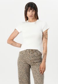 Top bianco a righe con maniche corte abbinato a jeans a vita alta con stampa leopardata, caratterizzati da un classico design a cinque tasche e chiusura con bottone.