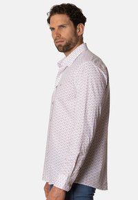 Camisa blanca con un pequeño patrón de hojas en tonos dorados, cuello estándar, botones en la parte delantera y mangas largas. Textura de tela suave.