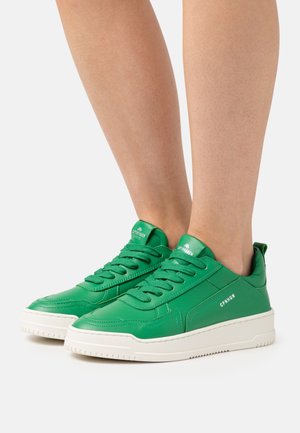 Grüne Leder-Sneaker mit einer weißen Gummisohle, ausgestattet mit flachen Schnürsenkeln, seitlichen Nähten und Branding auf der Zunge und der Ferse.