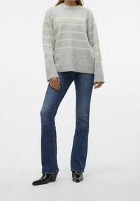 Maglione a righe grigie con strisce giallo chiaro, abbinato a jeans blu a campana e stivali neri con tacco, esposto su uno sfondo bianco.