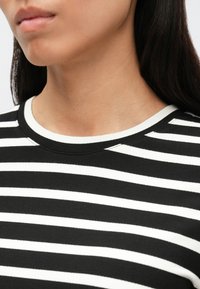 Čierno-biele pruhované tričko s okrúhlym výstrihom, vyrobené z mäkkej tkaniny. Má striedajúce sa vodorovné pruhy a lem v jednofarebnom odtieni.