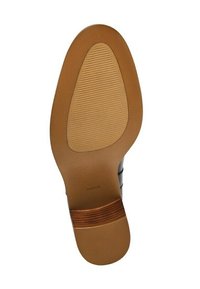 Suela de un zapato de vestir de cuero marrón con área de agarre texturizada y tacón de madera apilada, vista desde abajo sobre un fondo blanco.