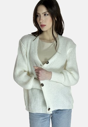 Witte gebreide cardigan met een V-hals, voorzien van twee grote knopen, geribbelde manchetten en een losse pasvorm. Draagt over een lichtbeige top.