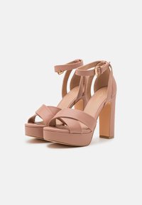 Sandales à talons hauts roses avec plateforme, caractéristiques de sangles croisées en tissu, de sangles à la cheville avec une boucle dorée et d'un talon bloc solide.