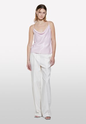 Camisola di raso rosa con scollatura drappeggiata, abbinata a pantaloni bianchi a vita alta con gamba larga. Il modello è in piedi contro uno sfondo neutro.