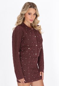 Burgundowa dziergana kamizelka z wzorem w warkocze, ozdobiona błyszczącymi srebrnymi koralikami i złotymi guzikami, zestawiona z pasującą spódnicą.