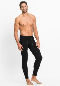 Schwarze Herrenleggings aus weichem Material, mit taillierter Passform, elastischem Bund und kontrastierenden Nähten auf der Vorderseite.
