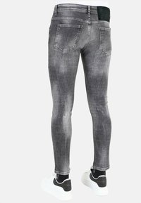 Strak passende grijze spijkerbroek met vervaging, twee achterzakken en een textuurafwerking, gecombineerd met zwart-witte sneakers.