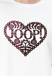 Tricou din bumbac alb cu un grafic în formă de inimă burgundă, detaliat cu modele florale și cuvântul „JOOP!” scris cu litere îngroșate.