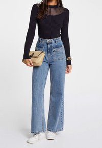 Marinblus med ribbat mönster och lång ärm med genomskinliga detaljer, hög midja ljusblå vida byxor och en vävd halmclutch. Vita sneakers fulländar looken.