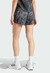 Juoksuhousut musta-harmaa kuviolla, joissa on teksturoitu muotoilu, yhdistettynä valkoisiin kenkiin ja sukkiin, nähtynä takaa.