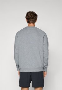 Sudadera gris con cuello redondo, mangas raglán y puños acanalados. Textura suave, vista desde la parte de atrás, combinada con pantalones cortos oscuros.