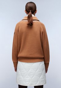 Bruine geribbelde gebreide trui met een brede kraag, gecombineerd met een witte gevoerde rok met een golvend patroon. Zichtbare naden en lange mouwen.