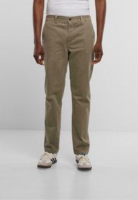 Chinos de algodón en twill color caqui con corte recto, bolsillos laterales y una textura sutil, combinados con zapatillas blancas y negras.
