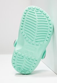 De mintgroene Crocs zool heeft een gestructureerd oppervlak met patroonlijntjes en circulaire accenten, gestempeld met de merknaam "crocs" en maat "C 5."