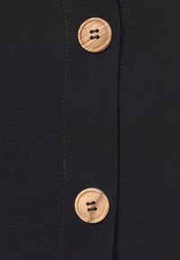 Schwarzer Stoff mit glatter Textur, der zwei runde Holzknöpfe aufweist, von denen jeder zwei sichtbare Löcher hat, die entlang der Seitennaht genäht sind.