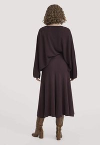 Burgundy knittitröja med lös passform, nedsänkta axlar och långa ärmar, tillsammans med en matchande långkjol och bruna knähöga stövlar.