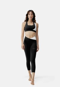 Melnas sporta krūšturis un leggings komplekts ar kontrastējošiem baltiem dizaina akcentiem, augstas elastības audums un pieguļoša siluets.