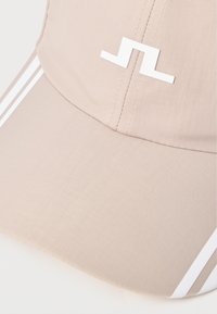 Bežna kapa z belim logotipom, z fino teksturo in dvema belima črtama ob straneh. Okrogla oblika s šivanjem.