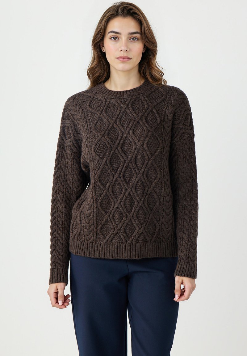 Brązowy sweter z dzianiny o teksturowanym wzorze diamentowym, okrągłym dekolcie i długich rękawach, zestawiony z ciemnoniebieskimi spodniami.