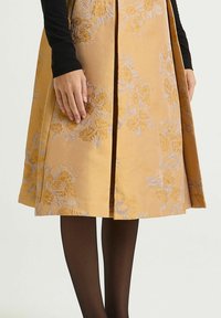 Une jupe mi-longue jaune moutarde ornée de broderies florales en or et lavande, avec une texture lisse et des plis latéraux.
