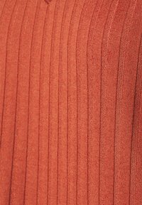 Débardeur en tricot couleur rouille avec une texture en côtes verticales. Le tissu est léger et lisse, avec un design en V.
