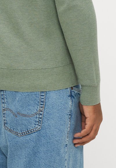 Πράσινο πουλόβερ με υφή πλέξης, με ριμπ μανσέτες και τελείωμα, σε συνδυασμό με φθαρμένο ανοιχτό μπλε τζιν παντελόνι με ραφές λεπτομέρειας στην πίσω τσέπη.