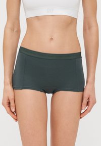 Calções de boxe em algodão verde-escuro com um ajuste justo, apresentando uma cintura macia com uma marcação discreta. Textura suave e design aerodinâmico.