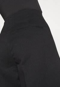 Czarne dopasowane spodnie charakteryzujące się eleganckim designem, teksturowanym materiałem oraz jedną tylną kieszenią z wąskim rozporkiem.