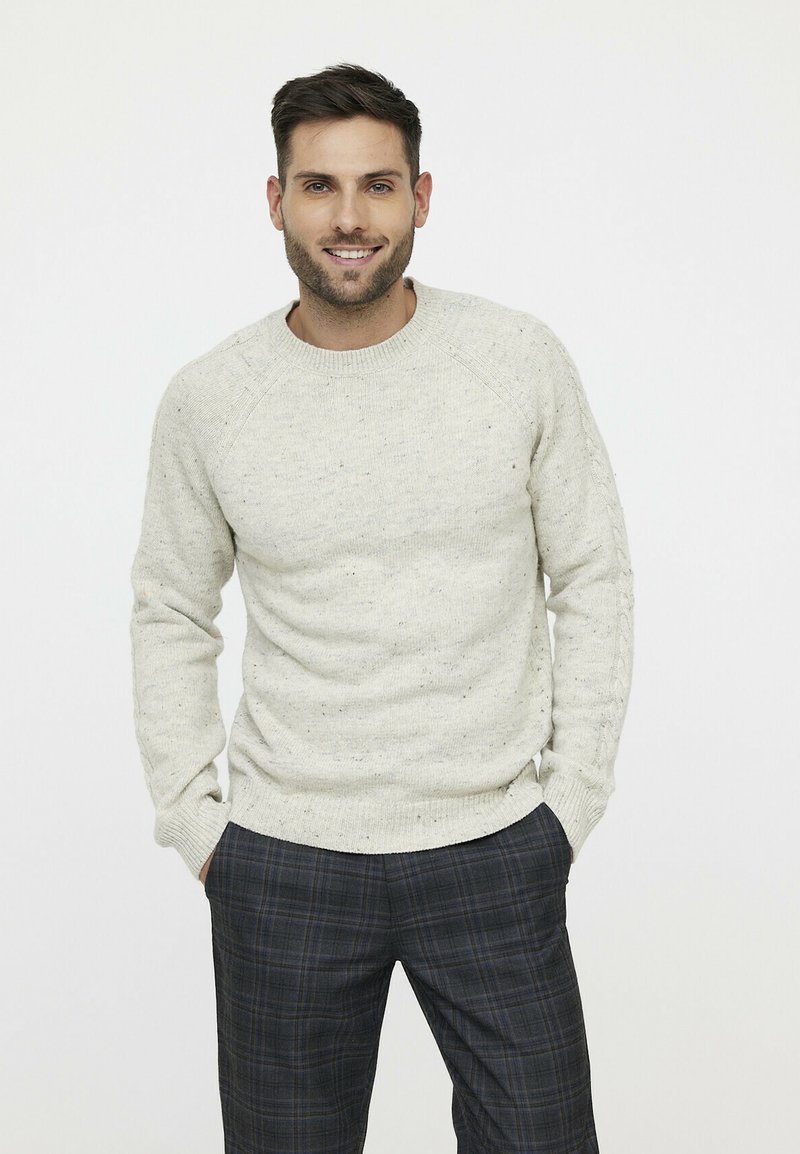 Helles graues gestricktes Sweatshirt mit Rundhalsausschnitt und gerippten Bündchen, kombiniert mit dunklen karierter Hose. Das Design weist ein gesprenkeltes Muster auf.