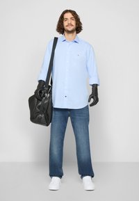 Lyseblå skjorte med oppbrettede ermer, blå jeans, svart lærveske med skulderrem og hvite sneakers. Svart hansker brukt.