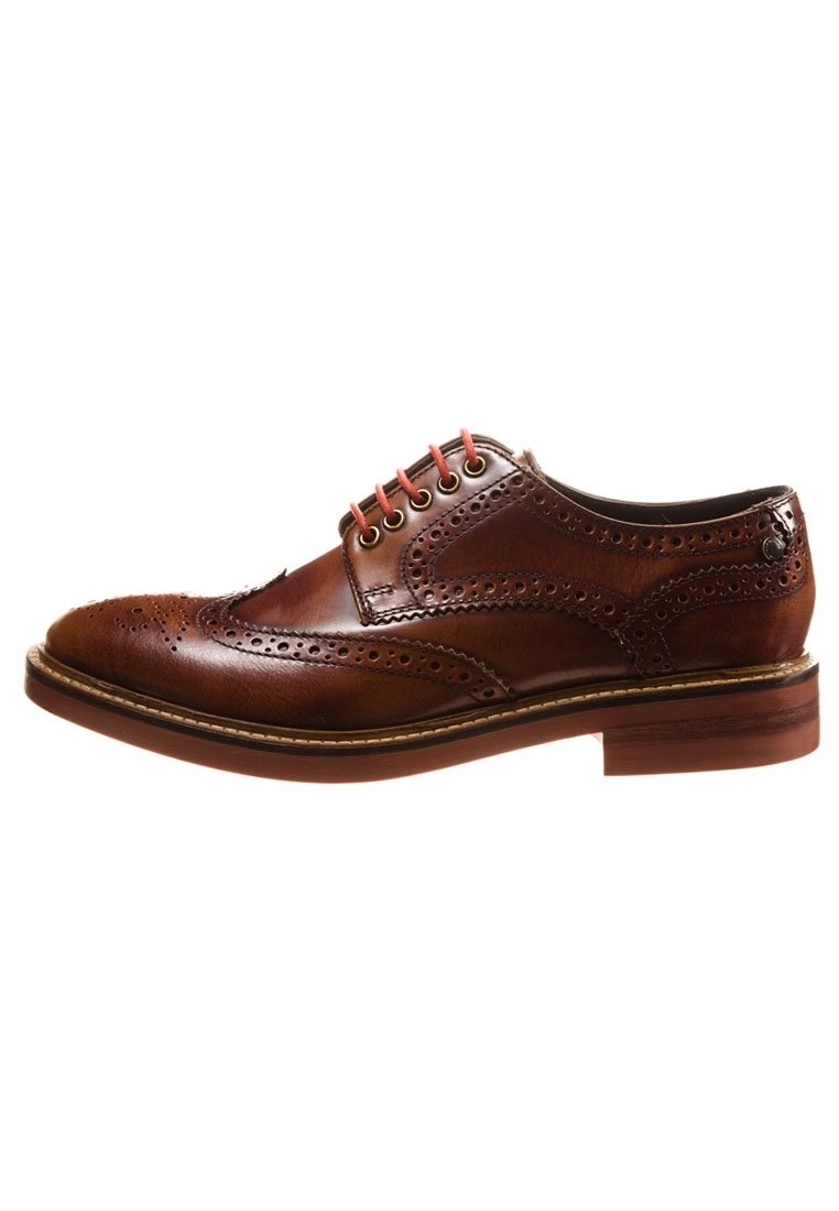 Chaussure en cuir marron avec un design brogue, dotée de perforations décoratives, d'un bout rond et de lacets rouges contrastants. Semelle robuste avec une texture minimale.