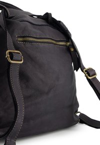 Czarna skórzana torba o teksturowej powierzchni, wyposażona w kieszeń na zamek błyskawiczny i kontrastowe beżowe przeszycia. Regulowany pasek i metalowe elementy.