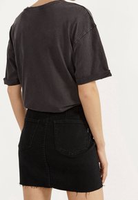 Zwarte oversized t-shirt met opgerolde mouwen, gecombineerd met een zwarte denim minirok met rafelige zoom en achterzakken.