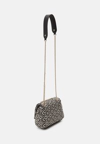 Small black and white diamond-patterned handbag with gold chain strap and short padded black leather shoulder pad hanging against white background.