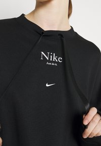 Svart sweatshirt med dragsko vid halsringningen. Har vit Nike-text och logotyp på bröstet. Mjuk tygkvalitet med avslappnad passform.