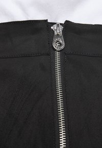 Tissu noir à texture lisse avec une fermeture éclair centrale argentée, contrastant avec le matériau, semblant faire partie d'un vêtement.