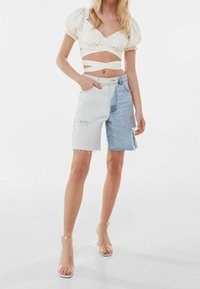 Szorty dżinsowe o wysokim stanie z białym i niebieskim wzorem w bloki kolorystyczne, postrzępione wykończenia oraz kontrastowe faktury. Noszone z krótkim topem.