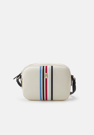 Kremowa prostokątna torba na ramię z pionowymi paskami w kolorach niebieskim, granatowym, białym i czerwonym oraz złotym logo, czarny regulowany pasek.